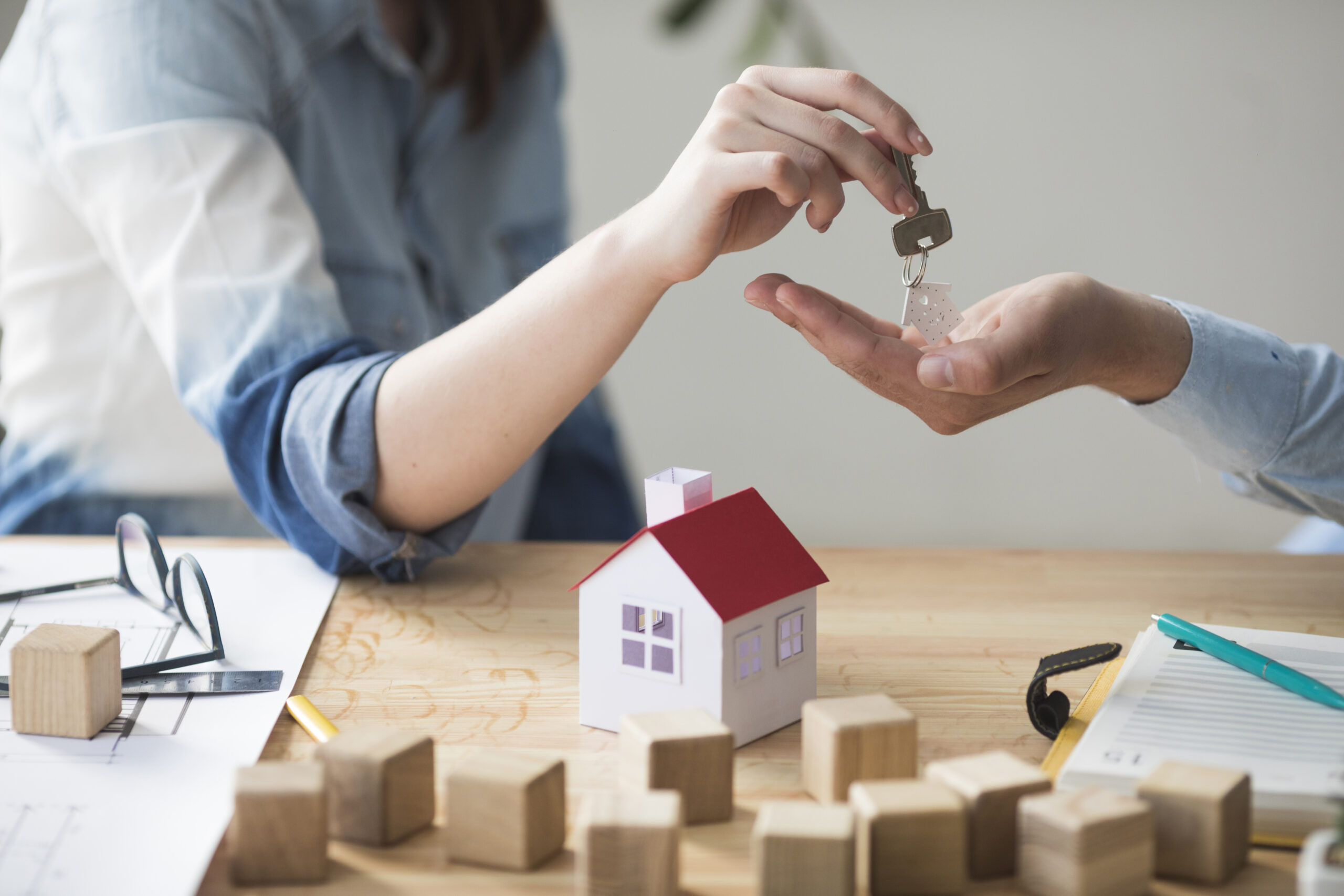 Photo des mains de deux personnes : l'une tend des clés à l'autre. Sous leurs mains, une maquette de maison posée sur une table pour illustrer la vente immobilière. Photo illustrant la formation loi ALUR de l'organisme de formation Tucetoo.